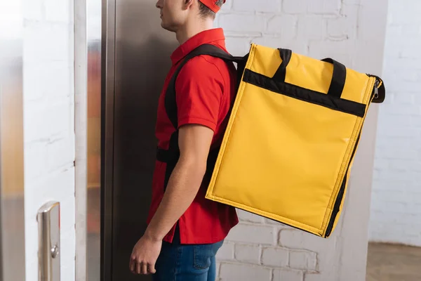 Vista cortada do homem de entrega com mochila térmica de pé perto do elevador — Fotografia de Stock