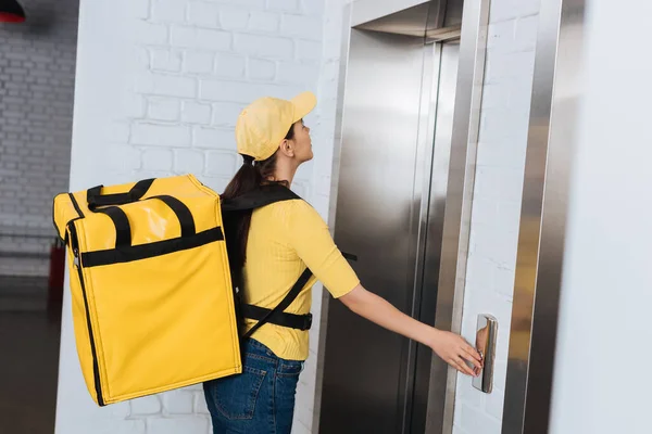Side view of courier with thermo backpack pressing elevator button — Stock Photo