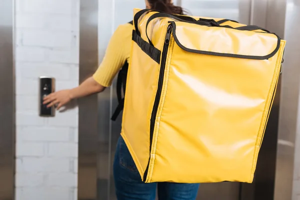 Selective focus of courier with thermo backpack pressing elevator button — Stock Photo