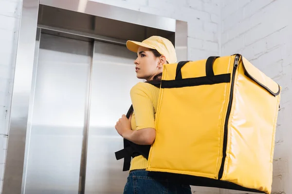 Back view of courier with thermo backpack standing near elevator — Stock Photo