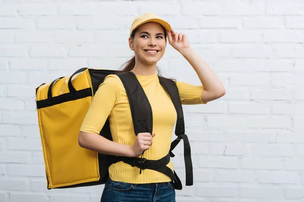 Courrier avec sac à dos thermique souriant près du mur de briques — Photo de stock