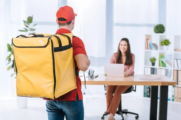 Back view of delivery man with thermo backpack and smiling businesswoman at table in office — Stock Photo