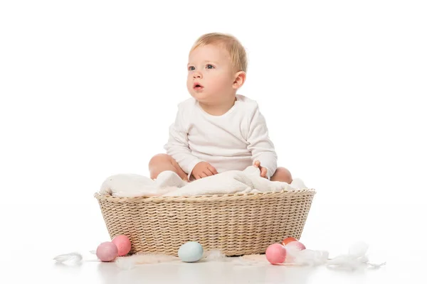 Child with open mouth sitting on blanket in basket with Easter eggs around on white background — Stock Photo