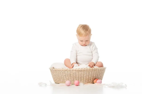 Child with lowered head on blanket in basket with Easter eggs around on white background — Stock Photo