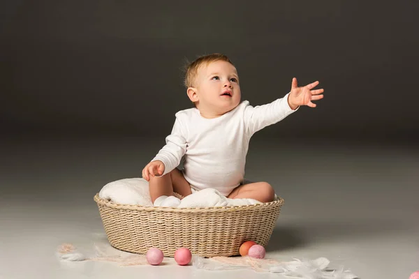 Criança com a mão estendida olhando para cima, sentada em cesta no fundo preto — Fotografia de Stock