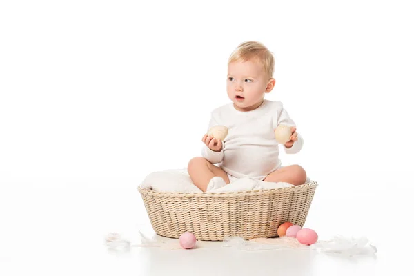 Enfant tenant des œufs de Pâques, regardant loin avec la bouche ouverte, assis dans le panier sur fond blanc — Photo de stock