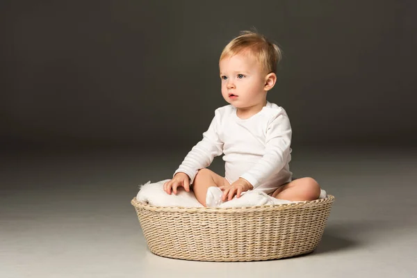 Lindo chico sentado en la manta en la cesta sobre fondo negro - foto de stock
