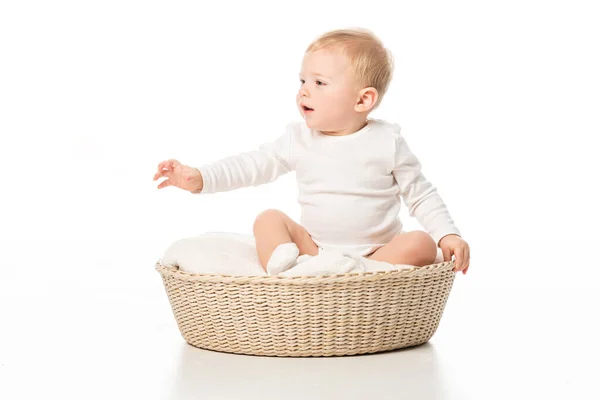Cute child looking away with outstretched hand and open mouth in basket on white background — Stock Photo
