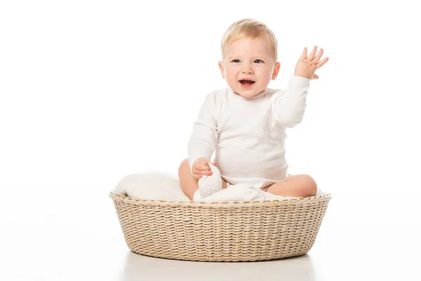 Niño con la mano levantada y la boca abierta, sentado en la manta en la cesta sobre fondo blanco - foto de stock
