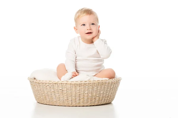 Enfant touchant le cou et levant les yeux, assis sur la couverture dans le panier sur fond blanc — Photo de stock