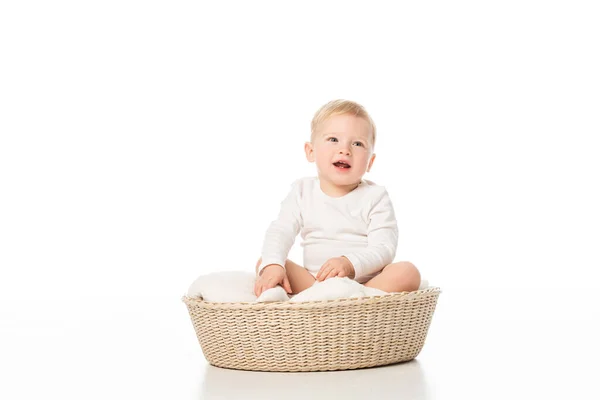 Lindo chico con la boca abierta sentado en la manta en la cesta sobre fondo blanco - foto de stock