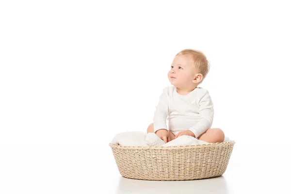 Cute child looking away and sitting on blanket in basket on white background — Stock Photo