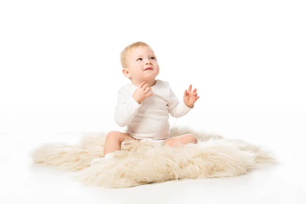 Lindo niño mirando hacia arriba y sentado en piel sobre fondo blanco - foto de stock