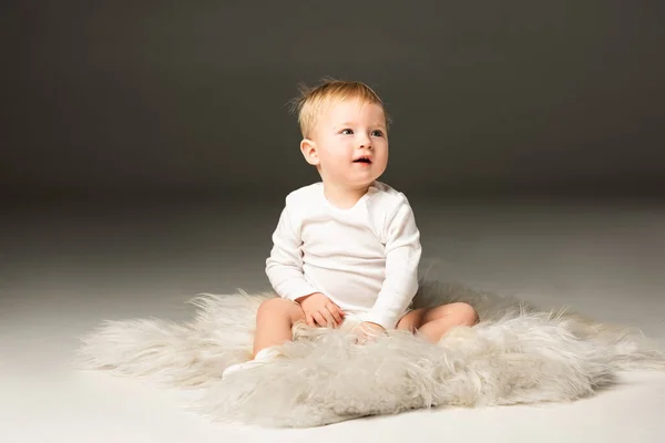 Cute child looking away with open mouth, sitting on fur on black background — Stock Photo