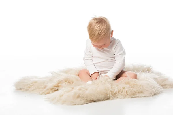 Criança bonito com a cabeça abaixada sentado na pele no fundo branco — Fotografia de Stock