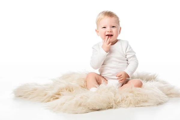 Cute child touching chin with open mouth, sitting on fur on white background — Stock Photo