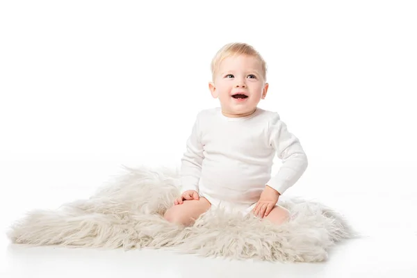 Mignon enfant heureux levant les yeux avec la bouche ouverte et assis sur la fourrure sur fond blanc — Photo de stock