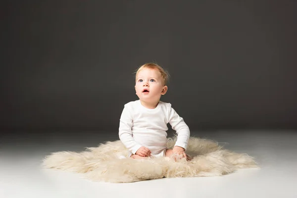 Cute kid looking up with open mouth, sitting on fur on black background — Stock Photo