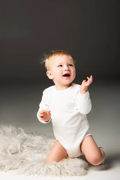 Cute happy kid looking up with open mouth, sitting on fur on black background — Stock Photo