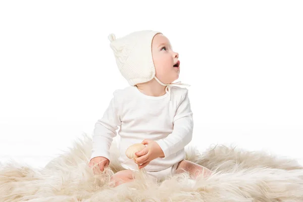 Kid wearing baby bonnet, holding easter egg, looking away with open mouth on fur isolated on white — Stock Photo