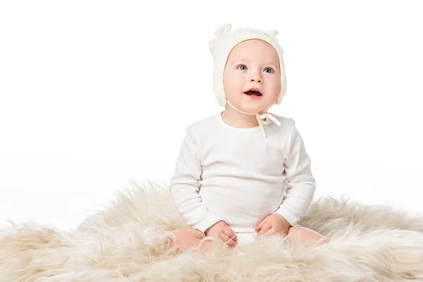 Child wearing baby bonnet, holding easter egg with open mouth, sitting on fur isolated on white — Stock Photo