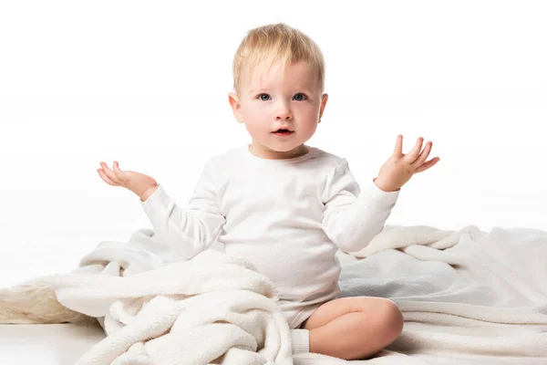 Niedliches Kind, das die Hände zur Seite spreizt und auf einer Decke auf weißem Hintergrund sitzt — Stockfoto