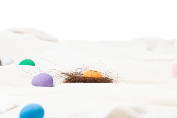 Selective focus of nest with yolk and colourful easter eggs on white blanket isolated on white — Stock Photo