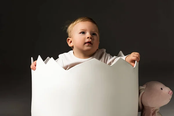 Child inside eggshell next to bunny isolated on black — Stock Photo