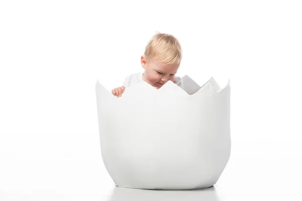 Criança bonito olhando para baixo dentro casca de ovo no fundo branco — Fotografia de Stock