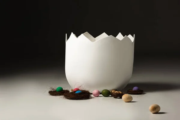 Empty eggshell next to easter eggs and nests on black background — Stock Photo