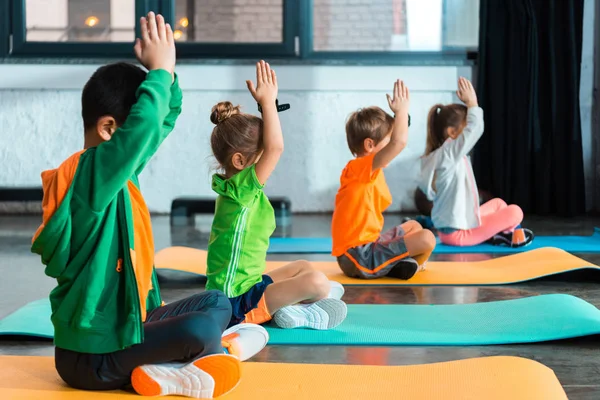 Enfoque selectivo de los niños con las manos apretadas que se estiran en las alfombras de fitness en el gimnasio - foto de stock