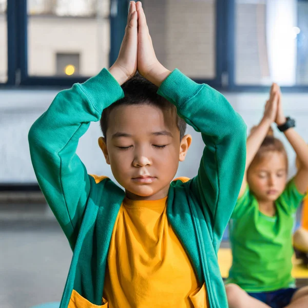 Selective focus of asian boy with clenched hands meditating in gym — Stock Photo