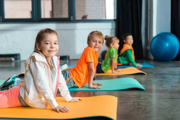 Focus selettivo dei bambini multiculturali che si allungano sui tappetini fitness in palestra — Foto stock