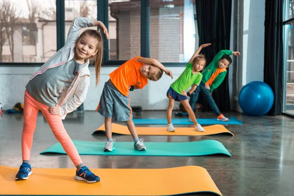 Focus selettivo dei bambini multiculturali che si riscaldano sui tappetini fitness in palestra — Foto stock