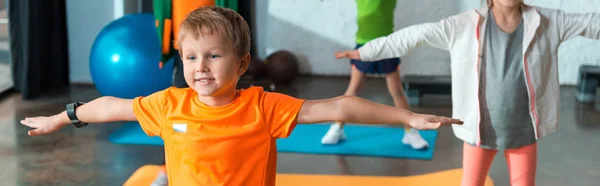 Vista recortada de los niños haciendo ejercicio con las manos extendidas en alfombras de fitness, plano panorámico - foto de stock