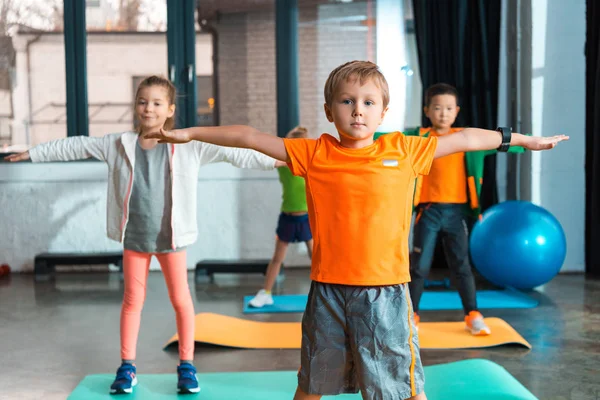 Foco seletivo de crianças multiculturais fazendo exercício com as mãos estendidas em tapetes de fitness — Fotografia de Stock