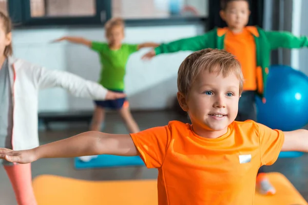 Selective focus of multiethnic kids doing exercise with outstretched hands in sports center — Stock Photo
