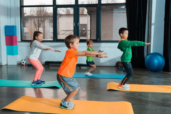 Enfoque selectivo de niños multiculturales en cuclillas con las manos extendidas en el gimnasio - foto de stock