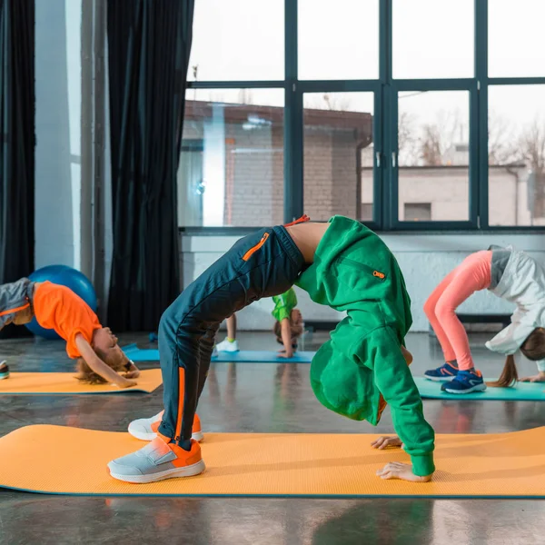 Enfoque selectivo de niños haciendo puente gimnástico en colchonetas de fitness en el gimnasio - foto de stock