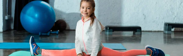 Enfoque selectivo del niño haciendo split en gimnasio, plano panorámico - foto de stock