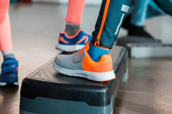 Vista recortada de los niños haciendo ejercicio en la plataforma de paso en el gimnasio - foto de stock