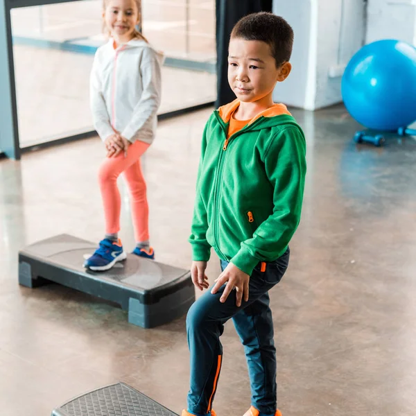 Concentration sélective des enfants multiculturels faisant de l'exercice sur les plates-formes pas à pas dans la salle de gym — Photo de stock