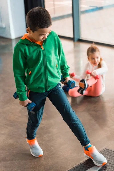 Selective focus of multicultural children holding dumbbells and working out in gym — Stock Photo