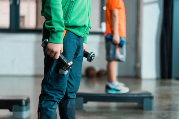 Vista recortada de los niños sosteniendo mancuernas, de pie sobre plataformas escalonadas en el gimnasio - foto de stock