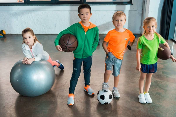 Kind liegt auf Fitnessball neben multiethnischen Kindern mit Bällen in Turnhalle — Stockfoto