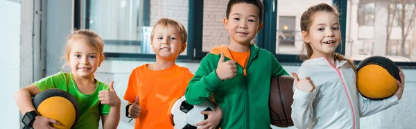 Front view of happy multicultural children holding balls in gym, panoramic shot — Stock Photo