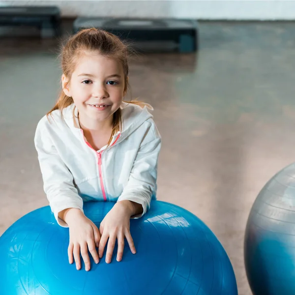 Selective focus of child smiling and leaning on fitness ball in gym — Stock Photo
