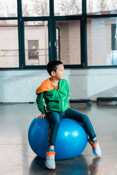 Selective focus of asian boy sitting on fitness ball in gym — Stock Photo