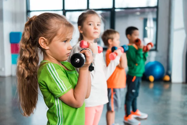 Focus selettivo di bambini multiculturali allineati, con manubri in mano nel centro sportivo — Foto stock