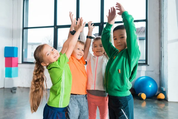 Multiethnische Kinder heben in Turnhalle gemeinsam die Hände — Stockfoto